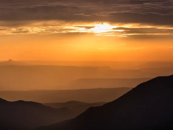 Photo of sunset through clouds over mountains.