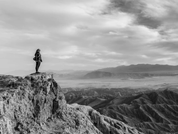 Person standing on a cliffside overlooking a vast mountain landscape