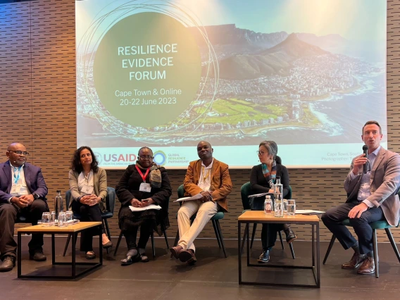 Conference panel being moderated with a presentation on display behind.